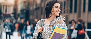 Eine junge Frau mit Büchern in der Hand lächelt.