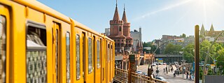 En gul metro kører over en bro i Berlin med en rabatkode til online sprogkurser i højre side af billedet.