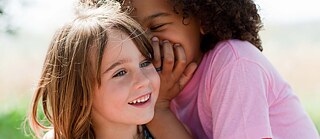 Deux enfants chuchotant l'un à l'autre et riant.