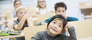 Die Schüler einer Grundschule sitzen im Klassenraum und verfolgen den Unterricht. Ein Mädchen hält ein Tablet in den Händen.