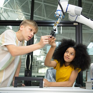 Zwei Kinder bauen einen Roboterarm.