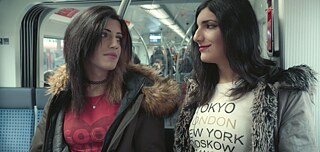 Two young women with long black hair on a train looking at each other