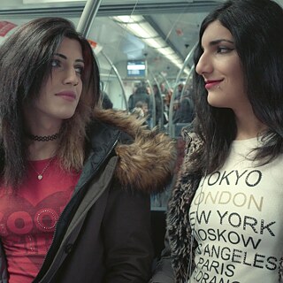 Two young women with long black hair on a train looking at each other