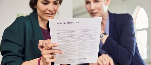 Gabriela hat die Prüfung bestanden. Sie hält das Goethe-Zertifikat B2 in der Hand und sichtet mit der Lehrkraft die Ergebnisse.