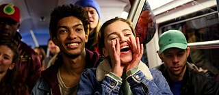 A woman in a blue denim jacket cheers enthusiastically for someone on the train.