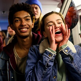 A woman in a blue denim jacket cheers enthusiastically for someone on the train.