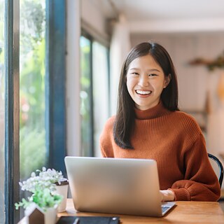 Eine Studentin sitzt an einem Schreibtisch mit einem Laptop in einem Café