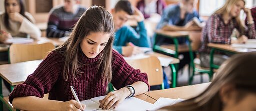 Schüler schreiben einen Test im Klassenraum. Der Fokus liegt auf einer Schülerin im Vordergrund.