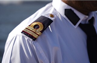 Detail picture of the insignia on the shoulder of a white military uniform. In the background the ocean. 