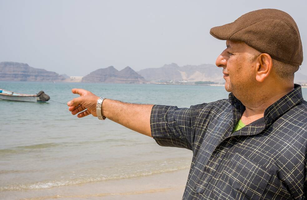 Kareem Hassan Mongy aponta para o antigo Porto de Al-Maala em Aden, no Iêmen, com o mar ao fundo.