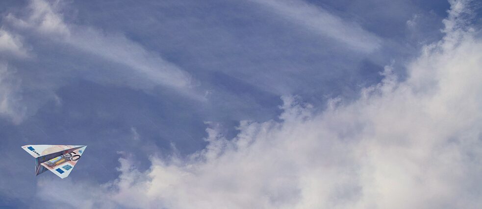 A paper airplane made from euro banknotes flies against a cloudy blue sky.