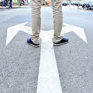 Event Header for Leading the Way to Germany: A man standing at an arrow road sign pointing in two directions