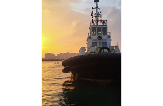 Part of a ferry at sea during sun down. In the background the silhouette of a city.