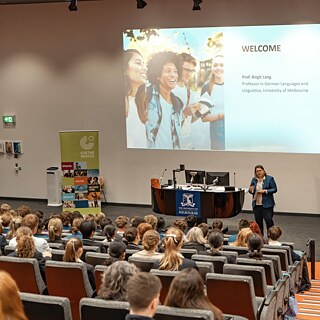 A woman confidently presents to a large audience, engaging them with her ideas and insights.