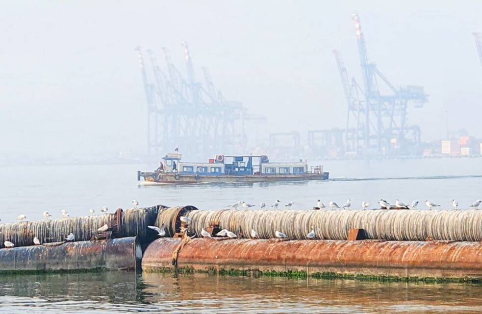 Balsa no meio do oceano em uma manhã de neblina. Ao fundo, um porto.