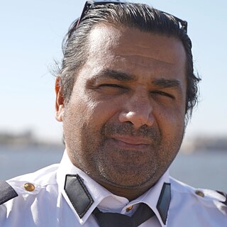 Wissam Hassan Al-Kawafi looks into the camera. Behind him you can see the ocean and the silhouette of the Port of Benghazi.