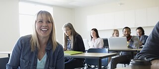 Erwachsene lernen im Klassenraum. Eine Frau schaut nach oben und lacht. 