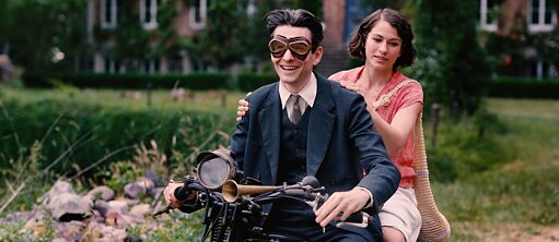 A man and a woman sit behind each other on a motorcycle in a rural setting