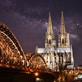 A stunning night view of the Cologne Cathedral and the Hohenzollern Bridge, illuminated against a starry sky, showcasing the iconic architecture and serene atmosphere.