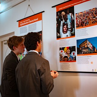 Two young men focused on a poster on the wall, discussing its details and exchanging ideas about the information presented.