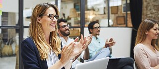 A woman in a meeting, clapping her hands with a joyful expression, celebrating a successful presentation or idea shared