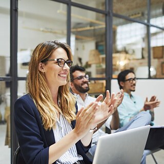 A woman in a meeting, clapping her hands with a joyful expression, celebrating a successful presentation or idea shared