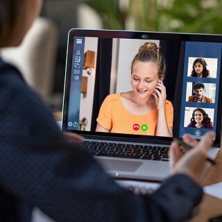 Gruppenonline-Kurs-Situation. Blick über die Schulter einer Kursteilnehmerin auf das Laptop mit Tatjana und weiteren Kursteilnehmern auf dem Screen.