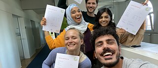 Selfie von Fero mit Tatjana, Sena, Noah und Amita. Sie stehen im Eingangsbereich des Goethe-Instituts und halten glücklich ihre Goethe-Zertifikate hoch.