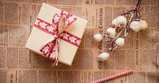 A small gift lies on an old newspaper, next to it a dried flower