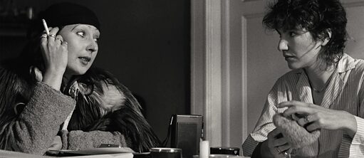 Filmstill: Two women in black and white sit smoking at a table