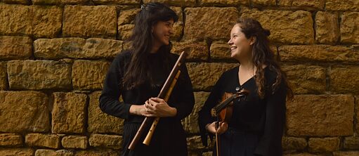 2 musiciennes se sourient devant un mur de pierres