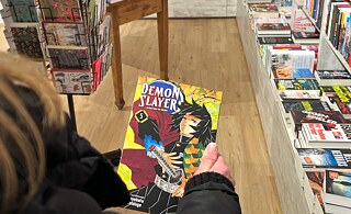 Woman carrying a book. In the background you can see that she is in a bookshop. 