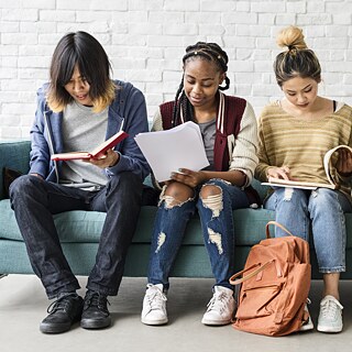 Mehrere junge Schüler sitzen nebeneinander auf einem Sofa und lesen.