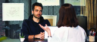 A person listens attentively to another individual speaking across a desk in an office setting.