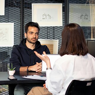 A person listens attentively to another individual speaking across a desk in an office setting.