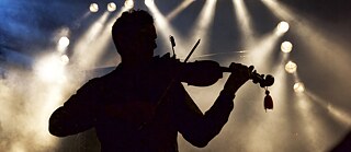 Ein Musiker steht auf der Bühne und spielt Geige. Silhouette im Gegenlicht.