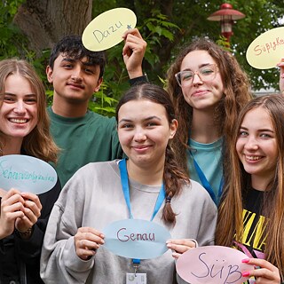 PASCH-Schülerinnen und PASCH-Schüler lächeln in die Kamera und halten bunte Zettel mit deutschen Wörtern nach oben.