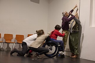 Szene mit Schauspielern und Schauspielerinnen an einer Wand