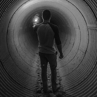 A person standing in a dimly lit tunnel, holding a flashlight that illuminates the space ahead.