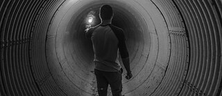 A person standing in a dimly lit tunnel, holding a flashlight that illuminates the space ahead.