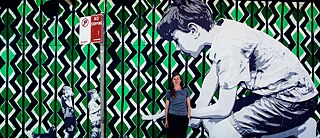 The Street Art Artist Mandy Schöne-Salter in front of her work ‘Imagine‘ (2015). This is a stencil and paste-up artwork created for the Avalon Art Carnival 2015. The work envisages the imaginary worlds children enter during playtime. 