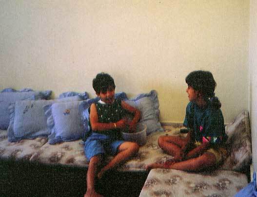 طفلان صغيران يجلسان على أريكة ذات تطريز مزهّر في منزل جديهما في غزة، فلسطين، العام ١٩٨٩.