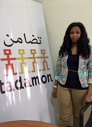 Fateema Idris, directrice exécutive du Conseil égyptien pour les réfugiés multiculturels (Tadamon), debout à côté d'un grand panneau sur lequel est écrit « Tadamon ».