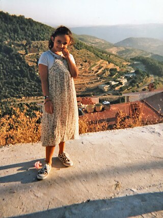 Huda Al-Jundi en tant que jeune fille, derrière elle un village en Syrie.