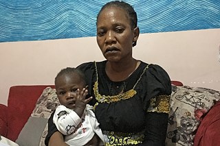 Rose Kuku auf einem roten Sofa mit ihrem Sohn auf dem Schoß