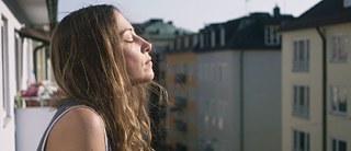 Janne (Aenne Schwarz) steht auf dem Balkon in der Sonne.