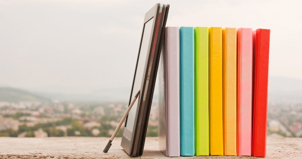 Bunte Bücher und ein E-Book-Reader auf einer Mauer