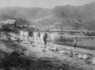 Kiautschou, German colony China: Beheaded Chinese (allegedly bandits) at the roadside, behind them Europeans have lined up for a group photo. Photo around 1900