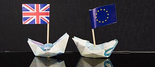 Two boats folded out of Euro banc notes; one with a flag of the EU, the other one with a UK-flag; black background