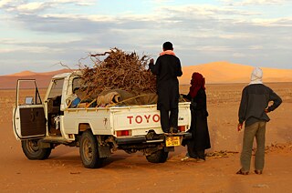 Latitude – Bedouin men loading a jeep with firewood in the Sahara desert, Libya